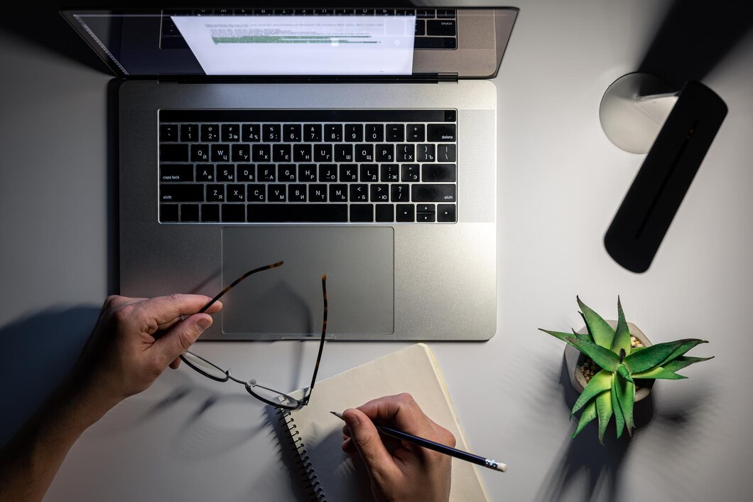 A top view of a workspace featuring a laptop, a desk lamp, and an organized desk in a dimly lit environment, conveying a focused, productive atmosphere